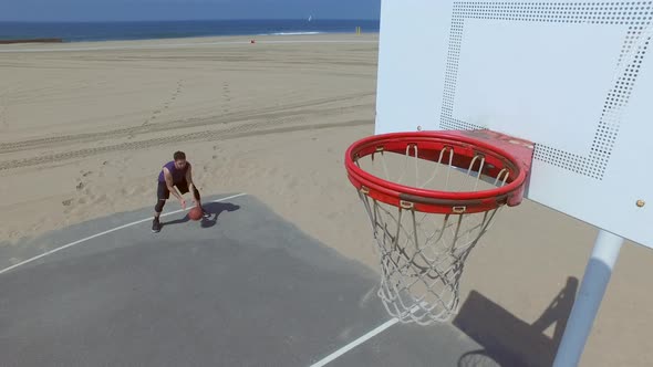 A man does a slam dunk while playing one-on-one basketball hoops on a beach court alt