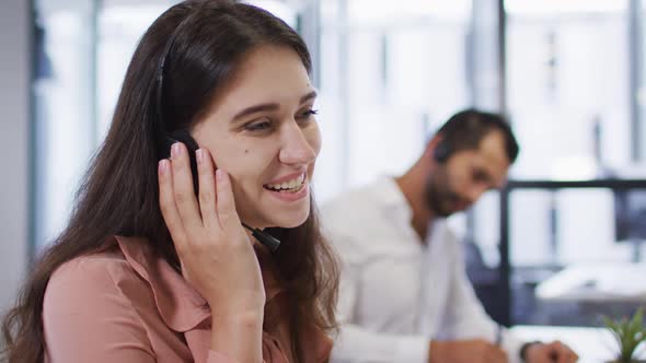 Portrait of caucasian businesswoman at office desk using phone headset and smiling to camera alt
