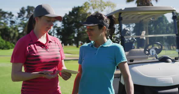 Two caucasian women playing golf talking writing in notebook alt