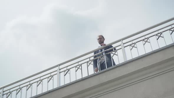 Wide Shot of Depressed Caucasian Businessman in Eyeglasses Approaching To Bridge Fence. Portrait of alt