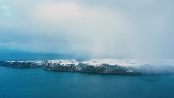A rocky uninhabited island covered in ice and snow in the open ocean.	