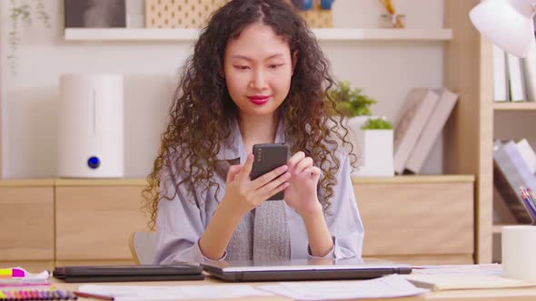 Happy Asian long curly hair woman scrolling on mobile phone at home office. Closeup joyful girl read alt