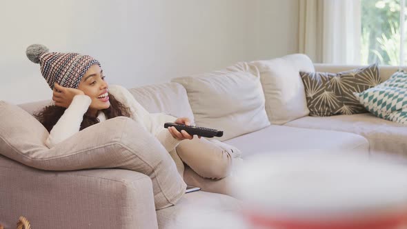 Happy woman in warm clothing lying on sofa watching television 4K 4k alt