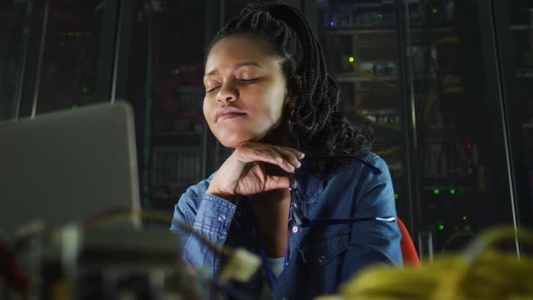 African american female computer technician using laptop working in business server room alt