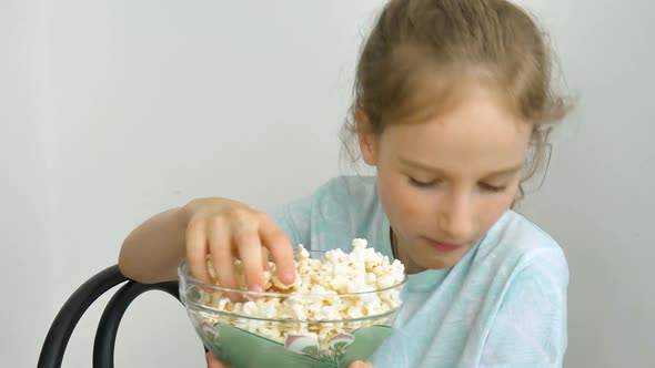 Portrait of a Funny and Excited Schoolgirl Girl on a White Background Smiling and Eating Popcorn alt