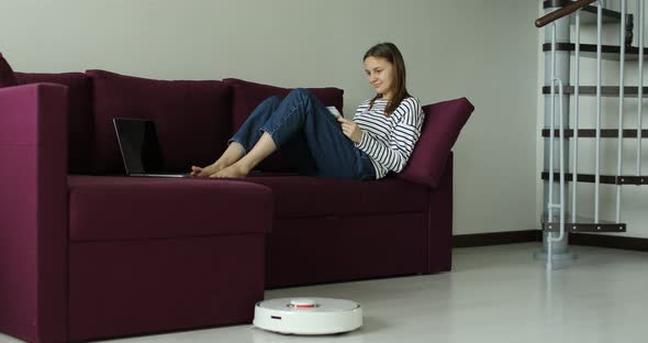 smart robot vacuum cleaner passes to clean the floor when woman working on sofa at home office. 