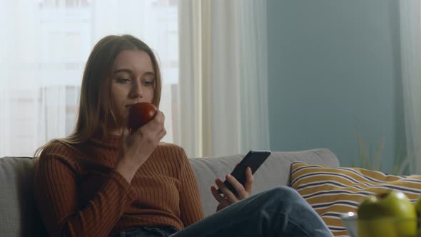 Pretty Lady Bites Red Apple and Looking at Something on Phone