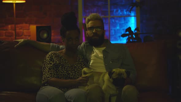Relaxed Young Diverse Couple with Dog Watching Tv on Sofa at Home alt