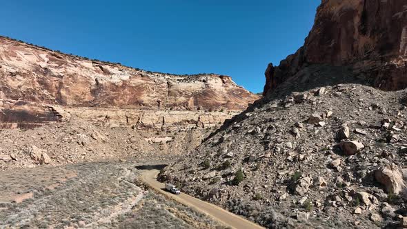 Flying through desert canyon as truck and trailer drive on dirt road in Utah alt