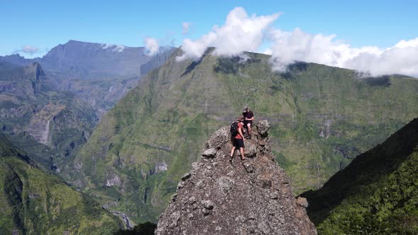 Drone footage of two people climing steep rock in front a scenery of the Cirque of Mafate at the Reu alt