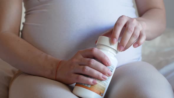 a pregnant woman takes vitamin pills by pouring capsules from a medicine bottle onto a woman's hand. alt