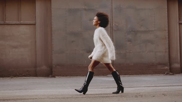 Smiling Young Woman With Windswept Afro Hair Walking Along Street alt