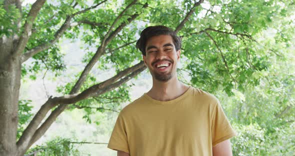 Portrait of cheerful biracial man in yellow t-shirt is standing against trees alt