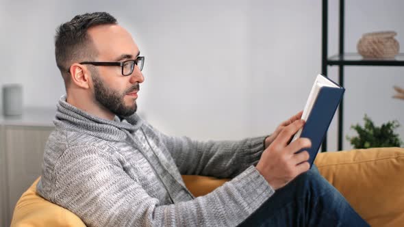 Handsome Bearded Guy in Glasses Reading Paper Text Book Lying on Couch alt