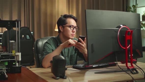 Asian Man Using Mobile Phone While Works On Personal Computer And 3D Printer In Home Office alt