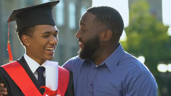 Extremely Happy Black Father Congratulating Son in Magisterial Suit, Graduation alt