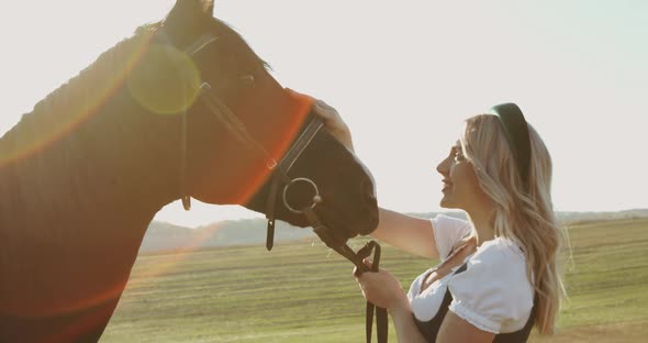 Girl in Has a Fun and Caresses a Brown Horse Among Wide Meadows with Sun Beams alt