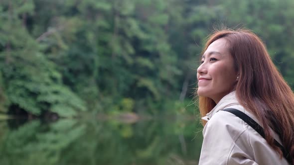 A young asian woman relaxing and looking at beautiful lake and green forest