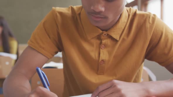 Mixed race boy writing in high school class alt
