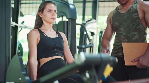 Asian Fitness trainer teach young sportswoman doing leg press exercise for muscle at gym stadium. alt