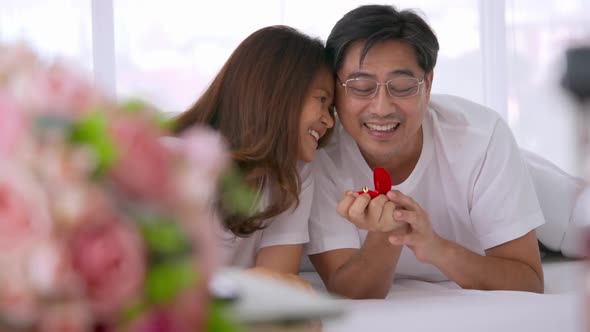 Asian man surprising his lover by giving a ring at the bedroom. alt