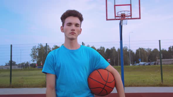 Serious Teenager with a Basketball Looking at the Camera at Sunset in Summer Day Cinematic