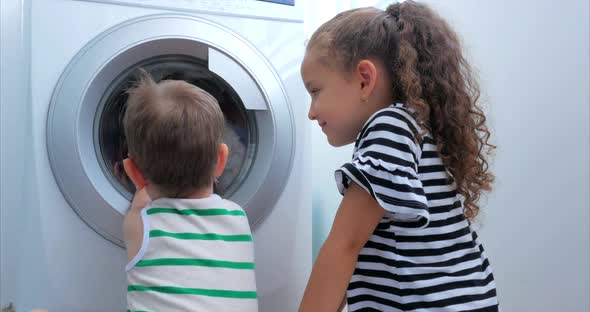 Cute Children Looks Inside the Washing Machine. Cylinder Spinning Machine. Concept Laundry Washing alt