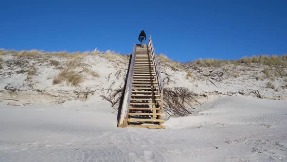 Man With Backpack Climbing Stairs To The Dunes