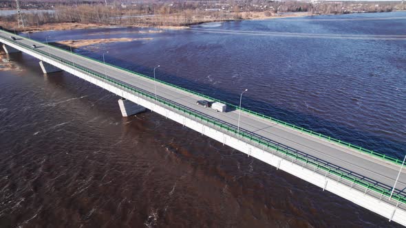 Concrete bridge over burgundy river due to impurities of snow in spring, cars drive across bridge