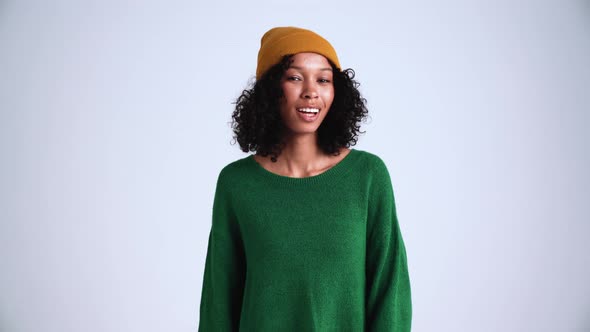 Positive curly-haired woman wearing hat saying yes at the camera alt