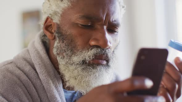 Senior man using smartphone while holding empty medication container alt