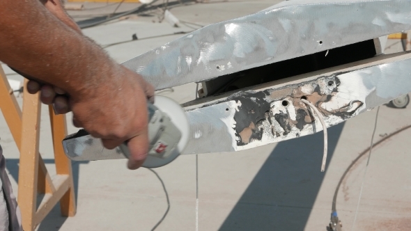 Worker Sanding Yachts Mast With Angle Grinder