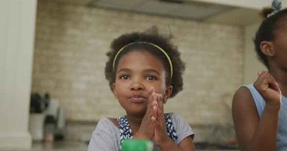 Happy african american girls eating and waving hands in kitchen alt