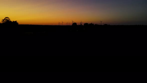 Wind turbines producing green energy. Windmill silhouettes in sunset. Aerial alt
