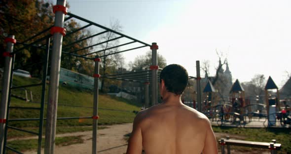 A Young Man Is Walking To the Sports Area and Pulling Up on the Bar in Sunny Weather  alt