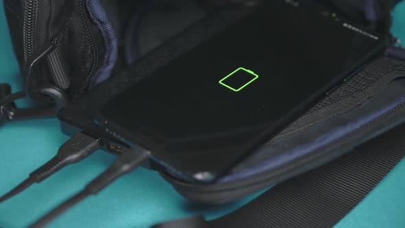 the phone is charged from a power bank lying on a backpack. Smartphone charging.