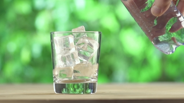 Water Pour On To Glass With Ice Cube On Wood Table