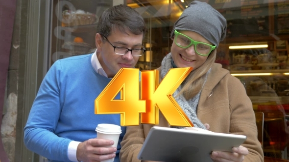 Young Couple Having Coffee And Using Pad In City alt