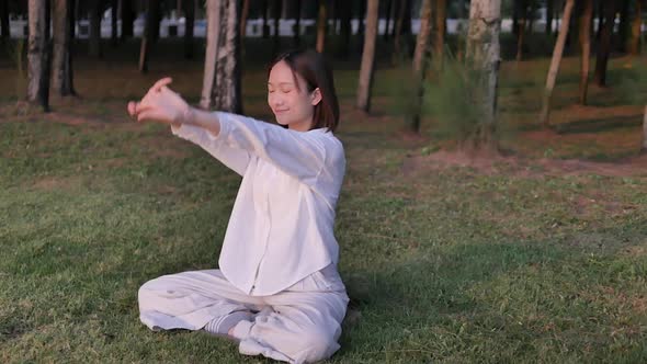 A meditative woman in casual clothes meditates with her eyes closed while sitting in a lotus pose