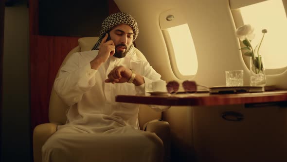 Smiling Businessman Talking Cellphone on Luxury Airplane in Muslim Clothing alt