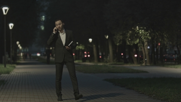 Businessman Talking By Phone While Walking In Park alt