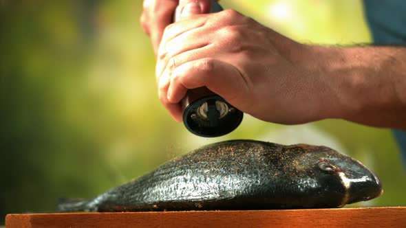 Seasoning Dorado Fish With Pepper And Salt On A Wooden Cutting Board In Slow Motion On Green alt