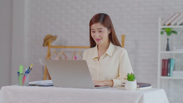 Portrait of beautiful business asian young woman working online with laptop and celebrating at home alt