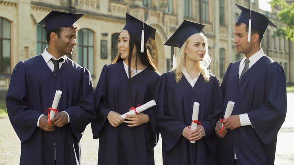 Graduate Students in Academic Regalia Talking and Looking Into Camera, Smiling alt
