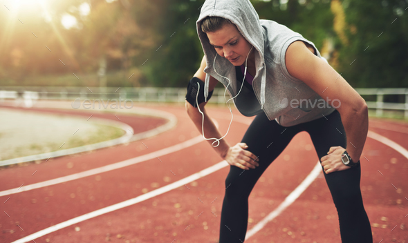 Fit young woman standing on track field and listening to music