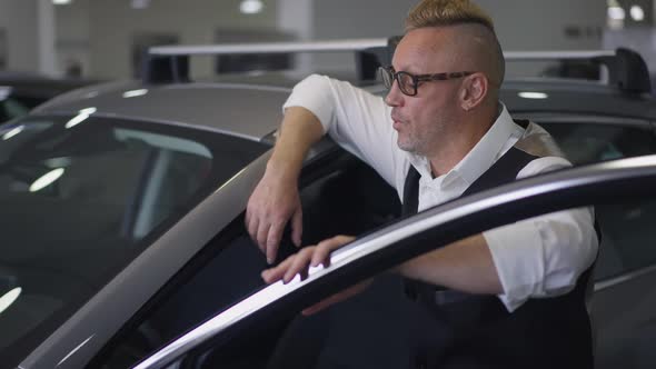 Side View of Man Admiring Brand New Car Touching Door Standing at Vehicle in Dealership alt