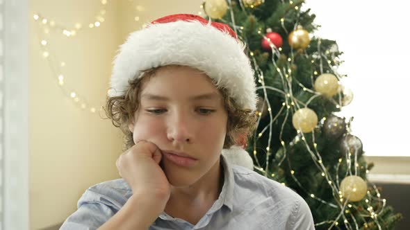 Portrait of a Teenage Boy Wearing a Santa Hat Who Is Bored or Sad. Against the Background of the alt