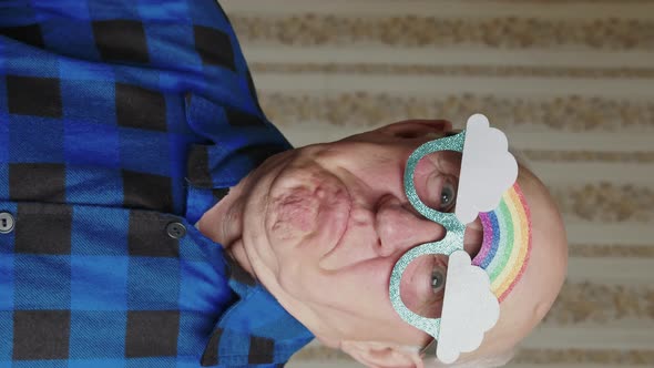 Funny Caucasian Old Single Man Wearing Paper Party Cartoon Glasses with Rainbow and Clouds on Them alt