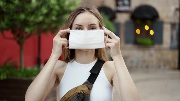 Woman Putting on Medical Mask for Coronavirus Protection Outdoors Front View alt