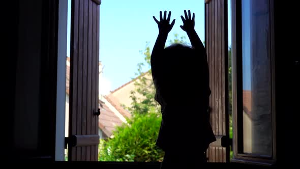 Silhouette of a Happy Girl Waving Her Hands on the Background of an Open Window alt